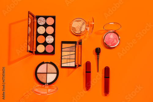 Beautiful palettes of eyeshadows and different decorative cosmetics on orange background photo