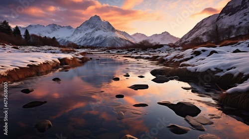 Dawn light bathes snowy mountains and a meandering stream with reflective waters, under a warm-toned sky.