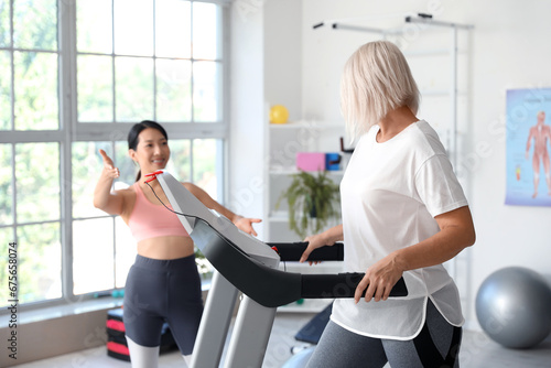 Mature woman training with therapist on treadmill in rehabilitation center