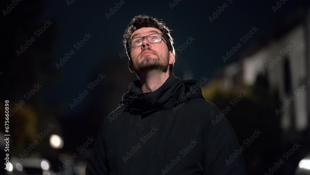 Young Man Enveloped in Cold German Suburb Night. Visible Breath and Backlit by Street Illumination, Stargazing. Visible european building style in the background. Man with beard and glasses. Young Man Enveloped in Cold German Suburb Night. Visible Breath and Backlit by Street Illumination, Stargazing. Visible european building style in the background. Man with beard and glasses.