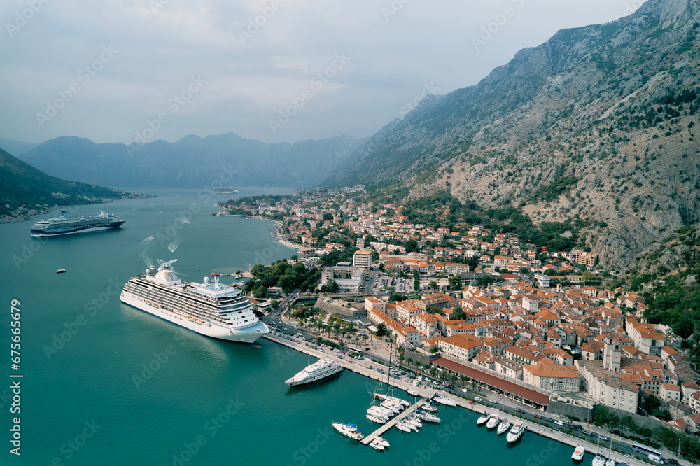 Large liner stands off the coast of an ancient town against the backdrop of mountains. Kotor, Montenegro. Drone