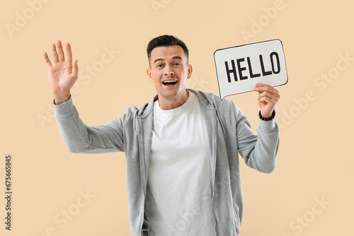 Young man holding paper speech bubble with word HELLO on beige background © Pixel-Shot