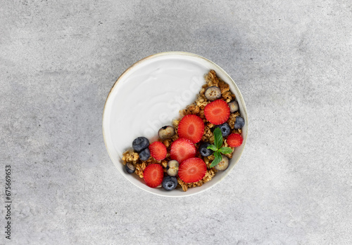 Yogurt bowl with granola and fresh berries: strawberries and blueberries on a gray background. Top view.