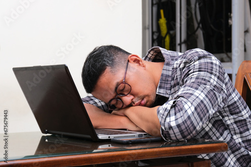 Adult Asian man sleeping in front of his laptop showing tiredness photo