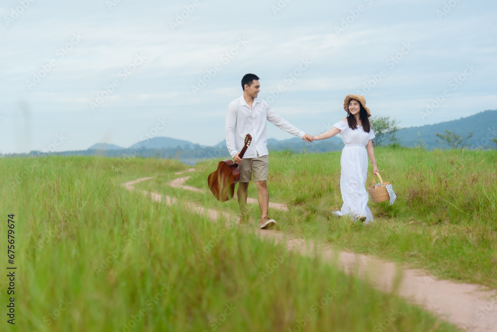 Obraz premium Asian man and woman couple walking in the middle of a meadow with a mountain background. morning sunlight