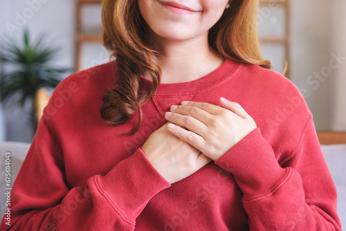 Closeup image of a happy young woman putting hands on her heart photo