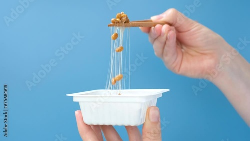 Female hand holding Japanese natto beans with wooden chopsticks on a blue background, side view. photo