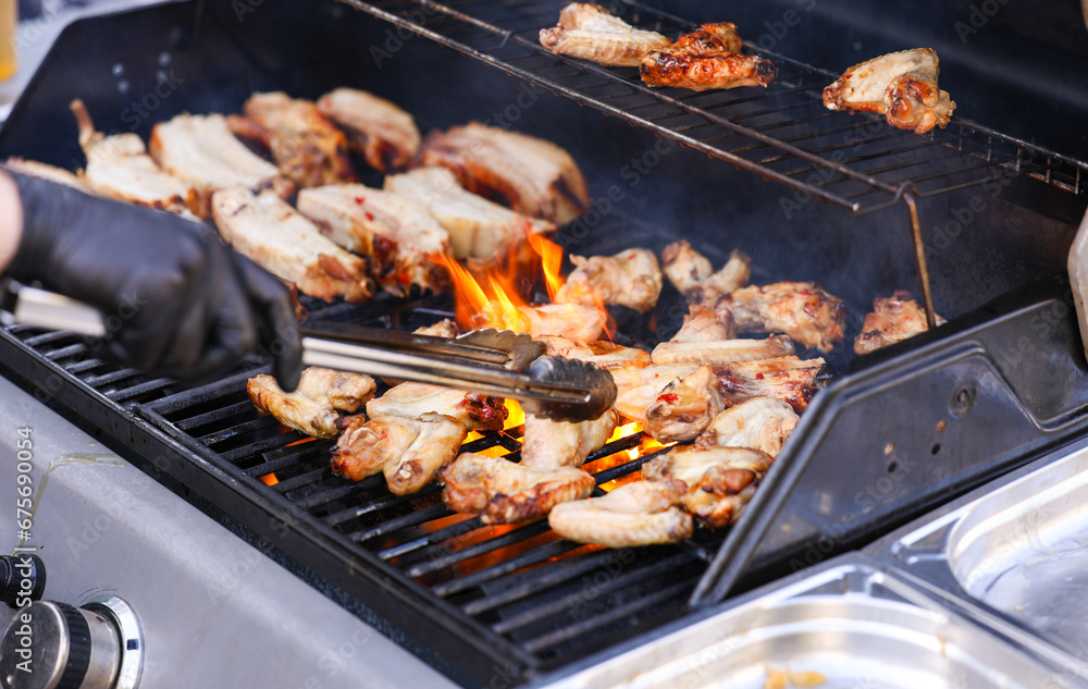 Outdoor barbecue party. Photo with the hands of a professional chef cooking pork and chicken wings over a gas barbecue grill.