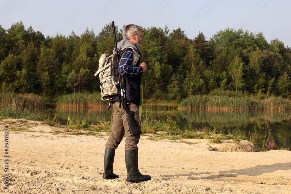 Naklejka premium Man with hunting rifle near lake outdoors. Space for text