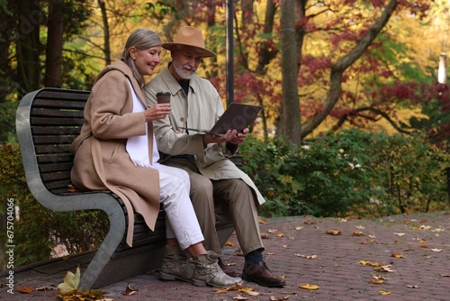 Fototapeta Naklejka Na Ścianę i Meble -  Affectionate senior couple with laptop spending time together in autumn park, space for text