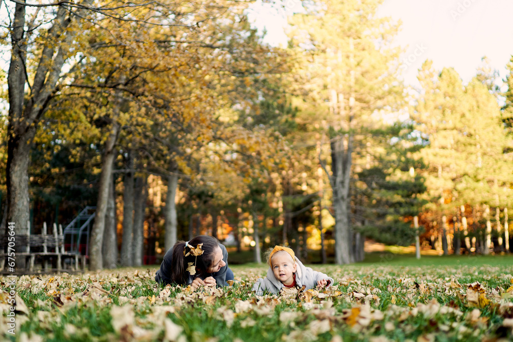 Mom with a little girl lie on their stomachs on the lawn among the fallen leaves