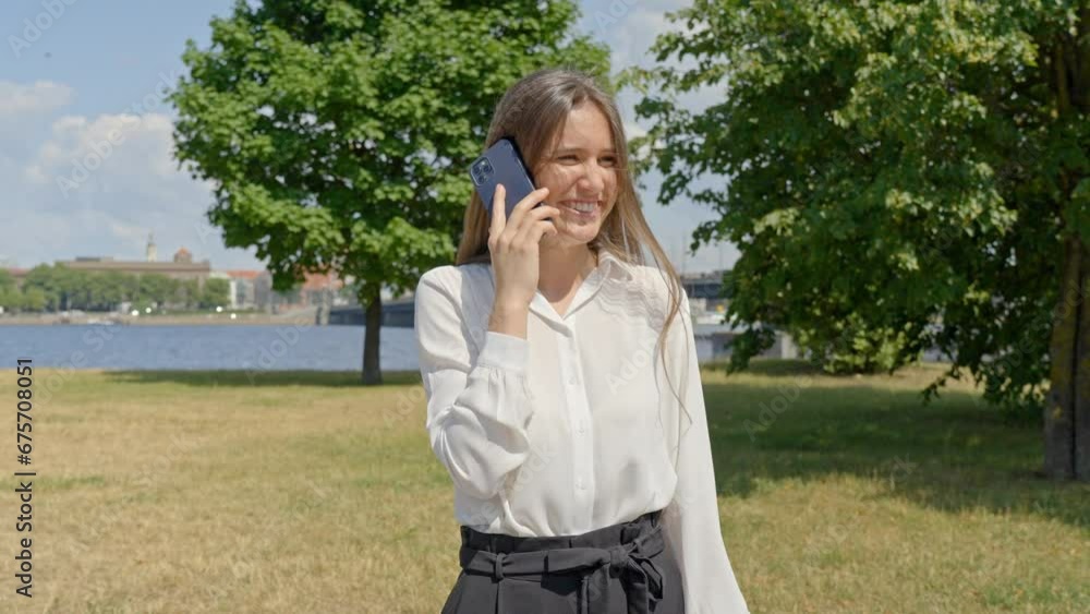 Stylish woman in park chatting on phone, blurry city in background Stylish woman in park chatting on phone, blurry city in background