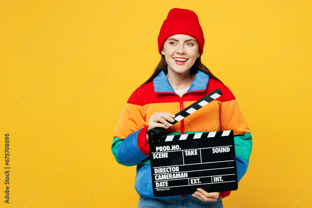 Full body young fun woman she wears padded windbreaker jacket red hat casual clothes hold in hand classic black film making clapperboard isolated on plain yellow background studio. Lifestyle concept. Full body young fun woman she wears padded windbreaker jacket red hat casual clothes hold in hand classic black film making clapperboard isolated on plain yellow background studio. Lifestyle concept.