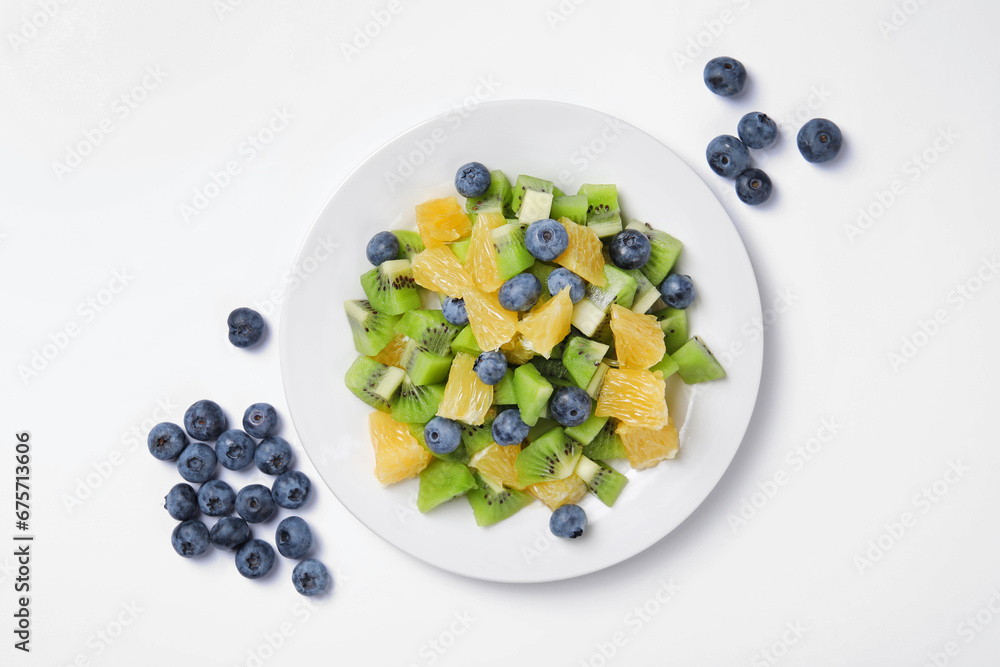 Plate of tasty fruit salad and blueberries on white background, flat lay