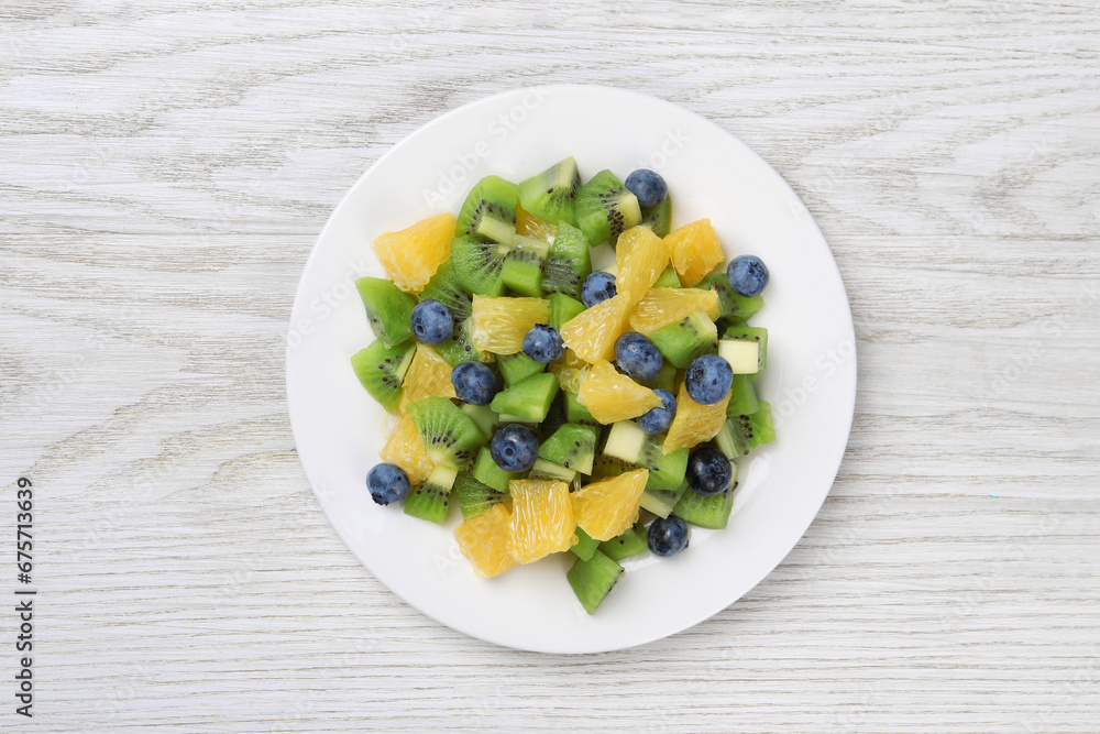 Plate of tasty fruit salad on white wooden table, top view