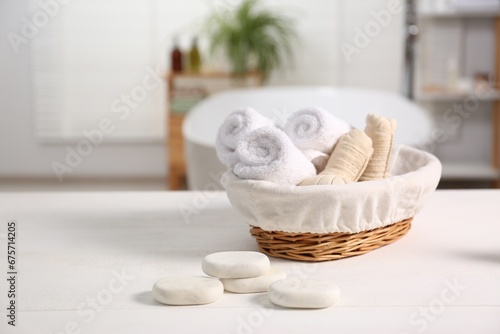 Basket with spa herbal bags, towels and stones on white wooden table in bathroom, space for text