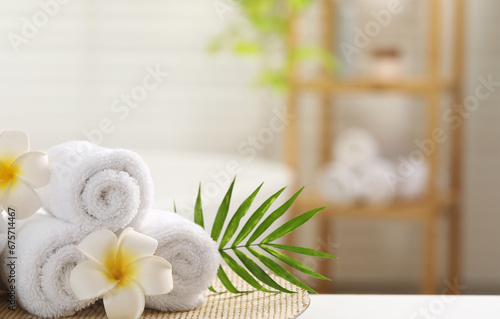 Spa composition. Towels, plumeria flowers and palm leaves on white table in bathroom, space for text