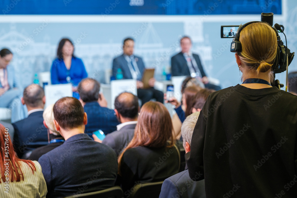 Obraz premium Back view of female videographer recording global conference meeting at export forum