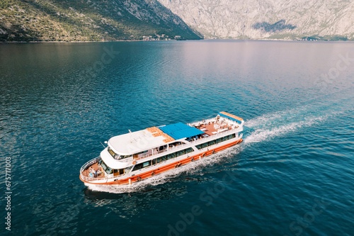 Colorful two-story ship with tourists sails on the sea along a mountain ridge