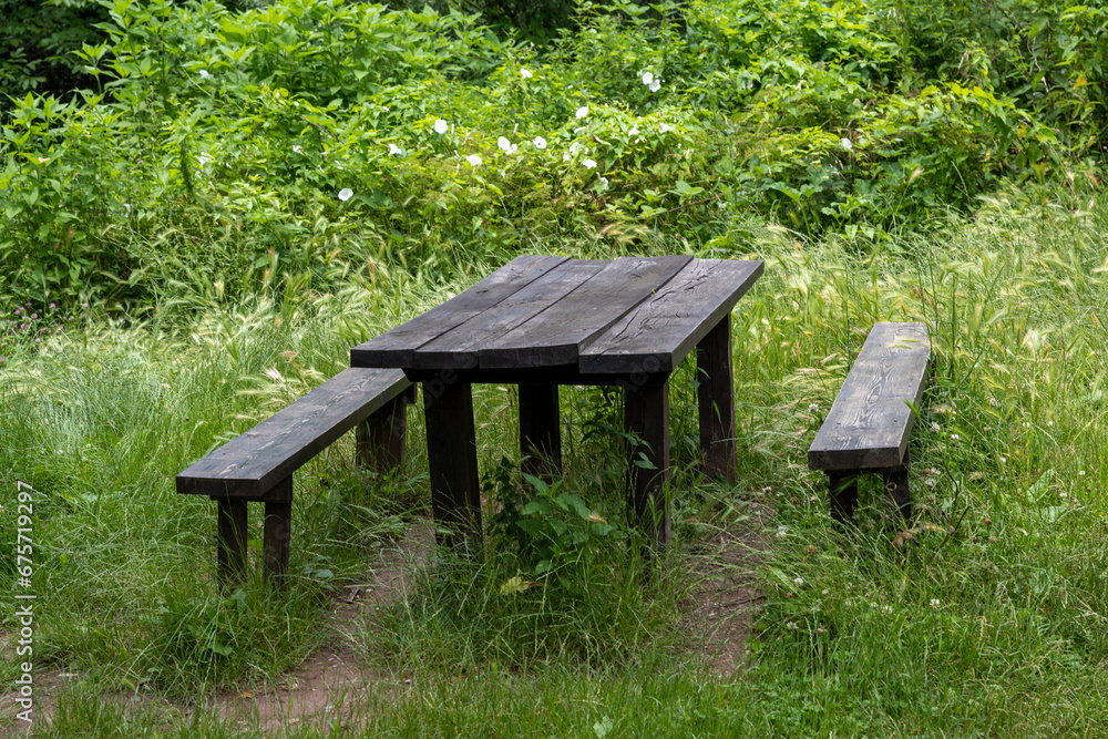 Two wooden benches and a large dining table in the forest. A place to rest in nature. Two wooden benches and a large dining table in the forest. A place to rest in nature.
