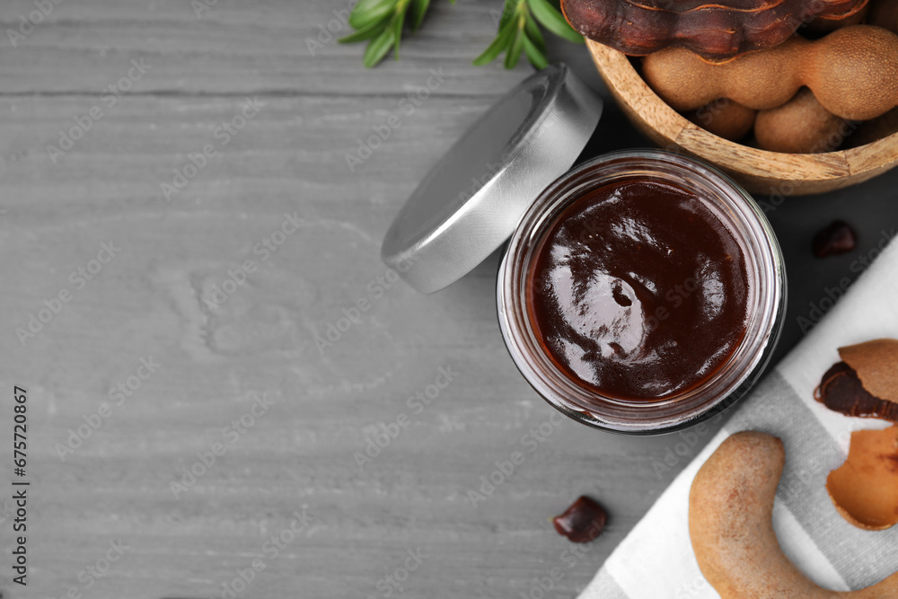 Jar of tasty tamarind sauce and fresh pods on grey wooden table, flat lay. Space for text Jar of tasty tamarind sauce and fresh pods on grey wooden table, flat lay. Space for text