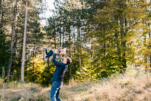 Dad throws up and catches a laughing little girl in a sunny forest © Nadtochiy