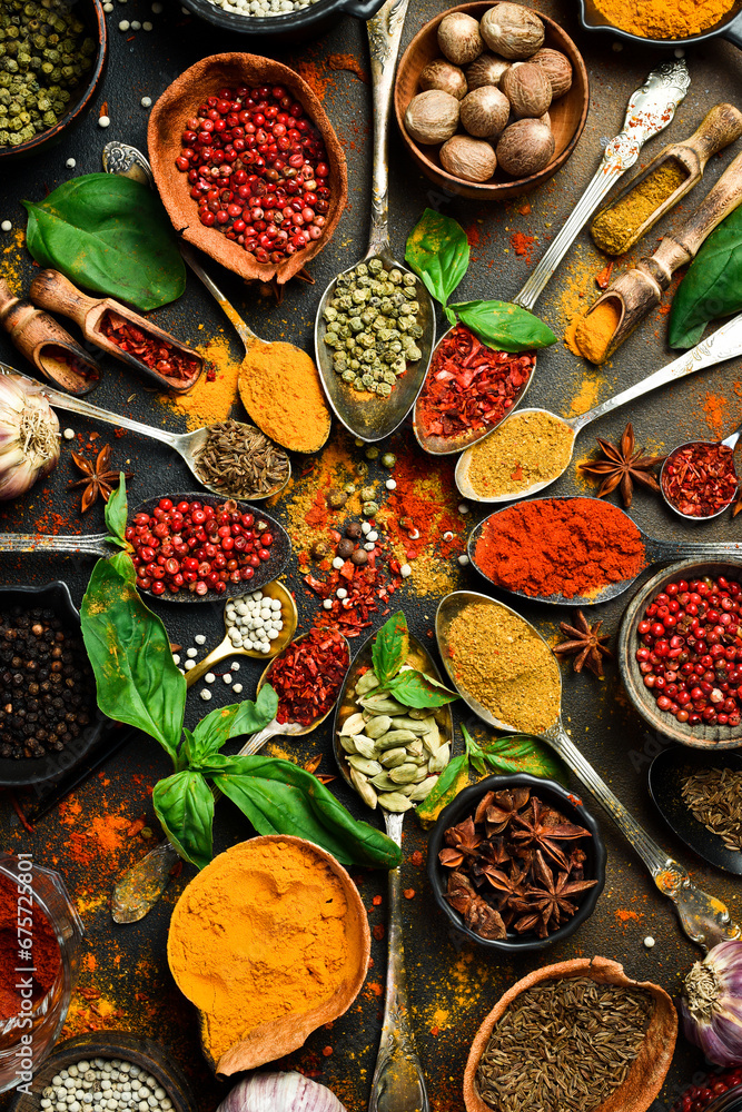 Colorful herbs and spices in spoons for cooking. Indian spices. On the background of black stone. Top view. - obrazy, fototapety, plakaty 