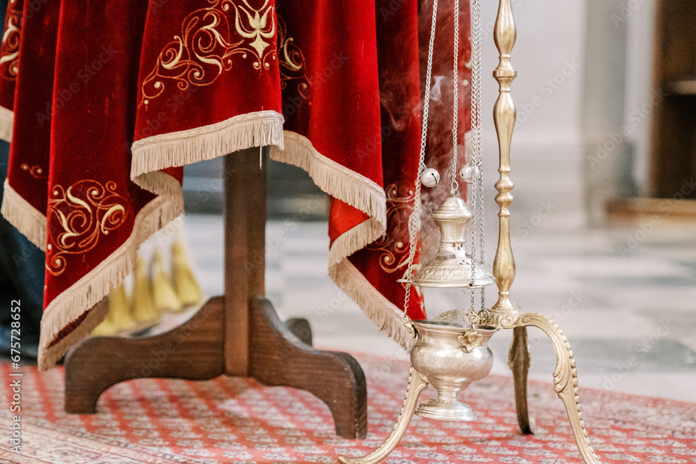 Smoking censer hangs on a gold chain on a stand near a table with a red tablecloth