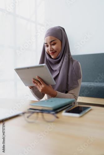 Female Muslim employee uses tablet to work at office. © Jirapong