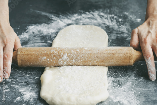 Rolls out the dough with a rolling pin a on concrete table. The process of preparing dough products. Production of cinnamon rolls or Cinnabon. Holiday baking