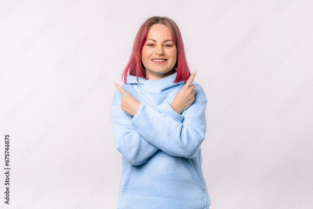Cheerful young woman with pink hair pointing fingers sideways, demonstrating banner or promo, showing logo, standing happy and smiling over white background Cheerful young woman with pink hair pointing fingers sideways, demonstrating banner or promo, showing logo, standing happy and smiling over white background