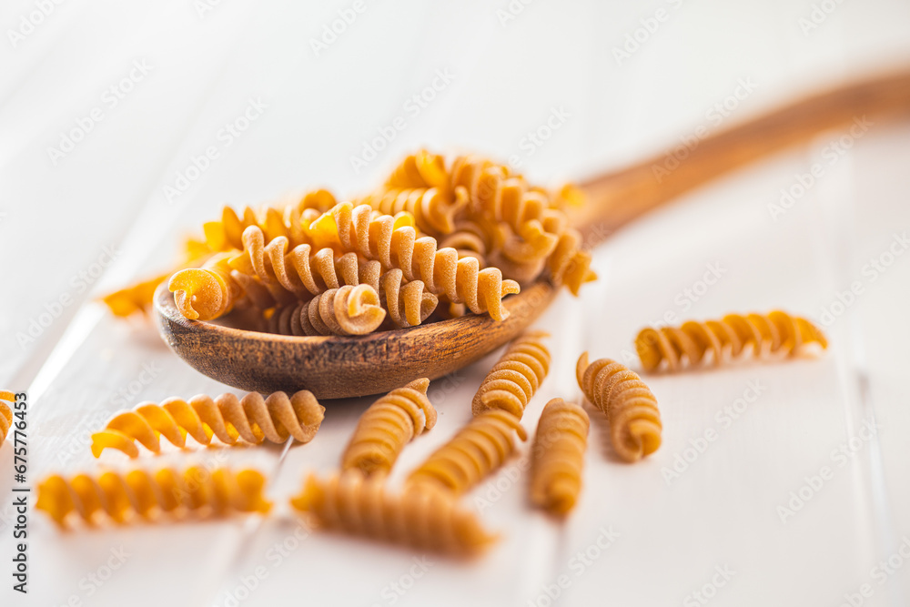 Naklejka premium Raw whole grain fusilli pasta. Uncooked pasta on wooden spoon.