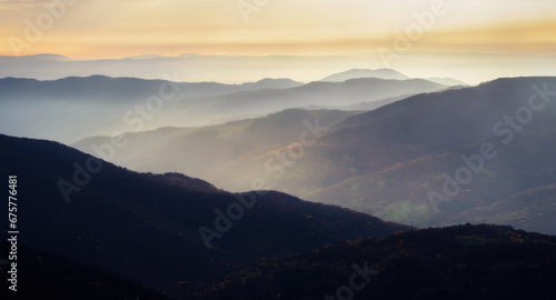 Mountain range with visible silhouettes through the morning colorful fog. Calm evening landscape in the mountains at sunset.Natural background. Panorama. Carpathian Mountains, Ukraine, Europe.