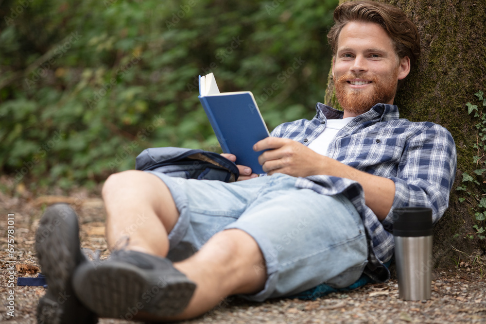 man resting in a park with a book and coffee