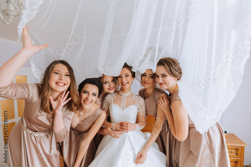 The bride in a white elegant dress poses with her girlfriends, covering herself with a veil