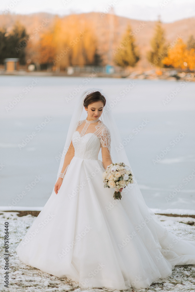 The bride holds a bouquet and poses during a walk in winter. Exquisite dress and hairstyle.