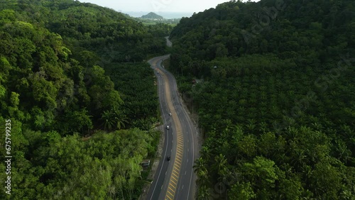 Aerial over a highway running through a tropical lush heavily jungled valley of limestone covered with palm trees near AO Nang, Krabi Province, Thailand. Drone dolly forward shot. photo