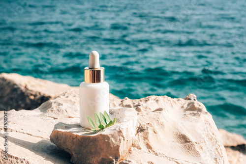 Cosmetic serum bottle on stone on the background of blue sea, closeup