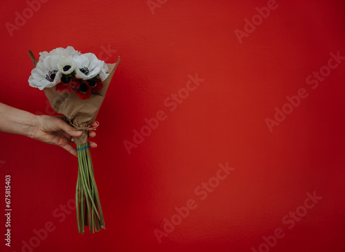 A bunch of flowers in brown paper is being held in front of a red door.