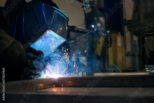 the male welder is dressed in protective clothing, he has a protective helmet on his head, he works in a locksmith workshop with a welding machine, he works with metal