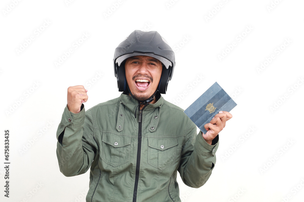 Happy asian man wearing helmet and jacket holding BPKB/Buku Pemilik Kendaraan Bermotor or Book vehicle owners from Indonesian police while clenching hand Happy asian man wearing helmet and jacket holding BPKB/Buku Pemilik Kendaraan Bermotor or Book vehicle owners from Indonesian police while clenching hand