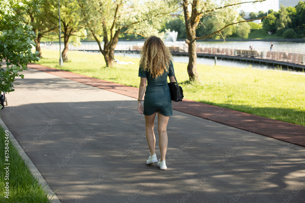 Girl walks through park in summer. Walk in summer on street. Shooting woman from back. Girl walks through park in summer. Walk in summer on street. Shooting woman from back.
