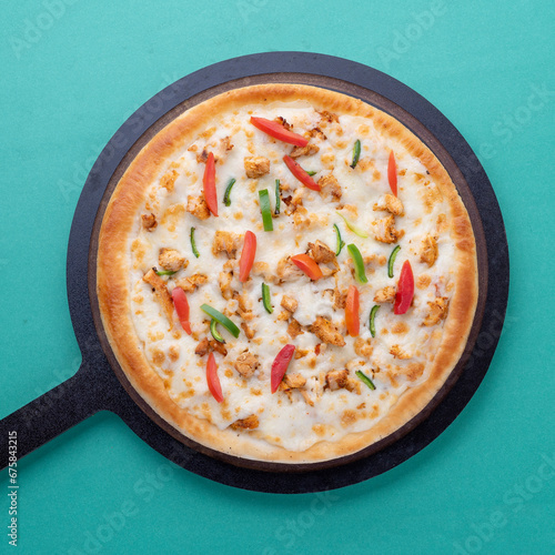 tomatoes and capsicum topping pizza with wooden pan on green background