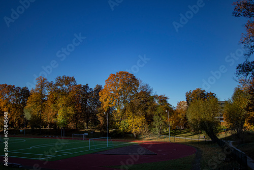 Autumn city park with colorful trees and a football stadium in foreground, copy space in clear blue sky