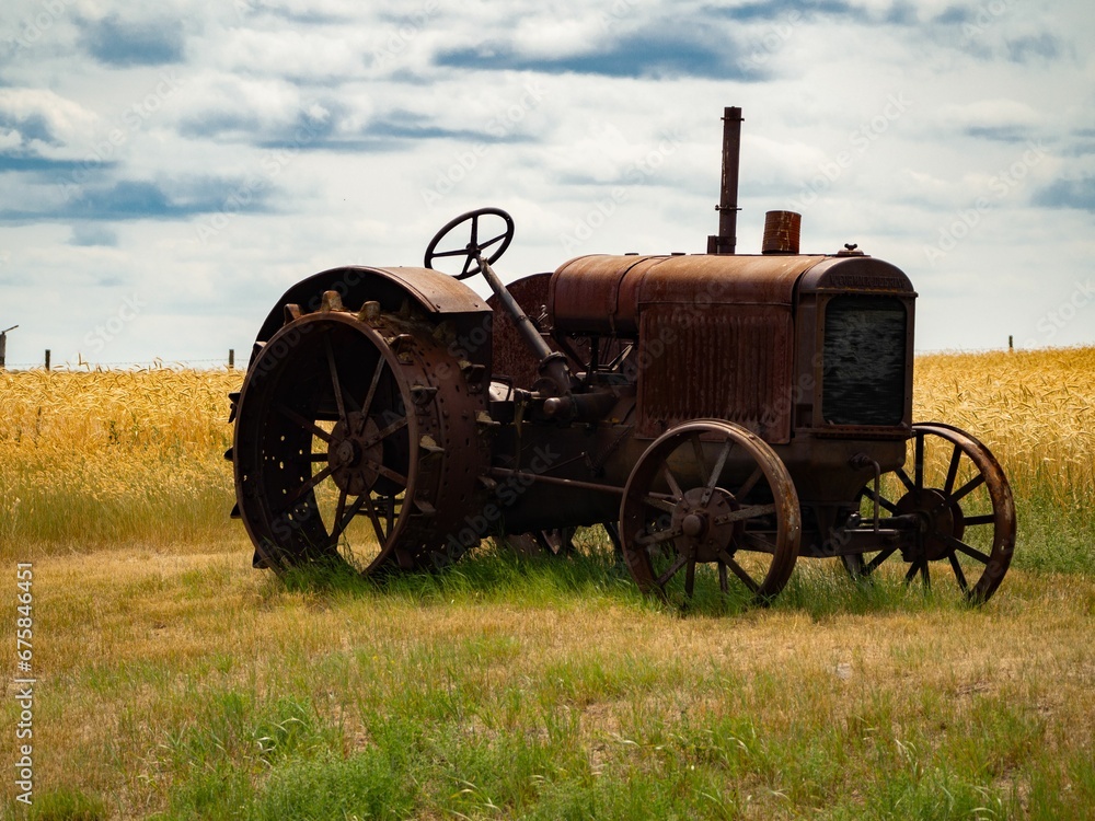 Obraz premium Vintage tractor parked in a field of golden grain, standing alone in the open countryside