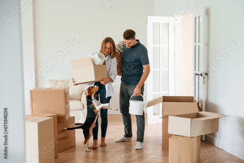 In the big room, with boxes in hands. Young couple with dog are moving to new home