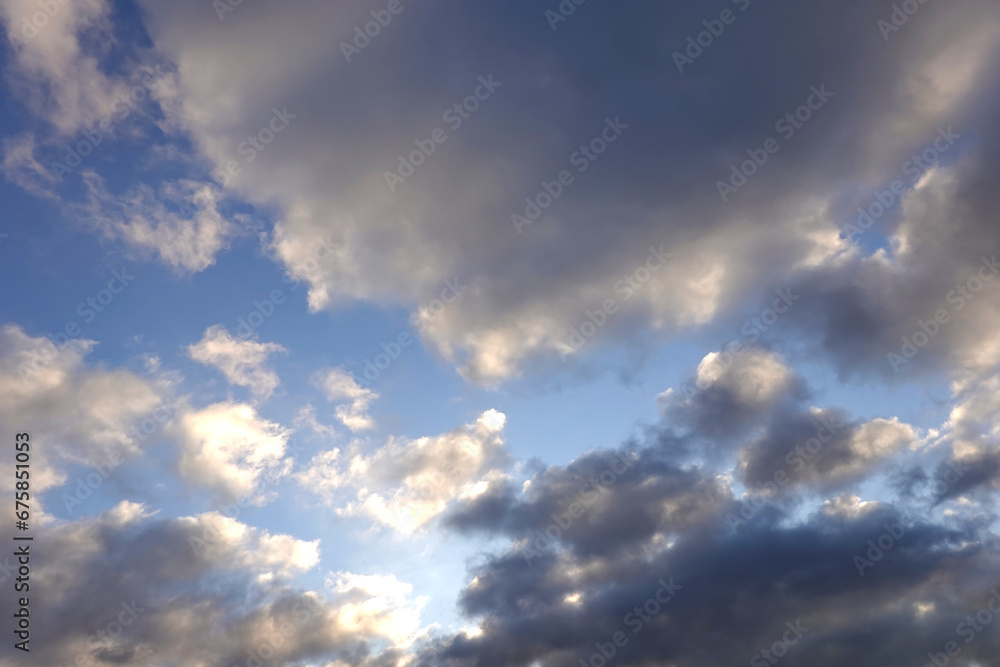 Beautiful heaven landscape with dense stormy white and gray clouds on different levels against the sun and some blue sky