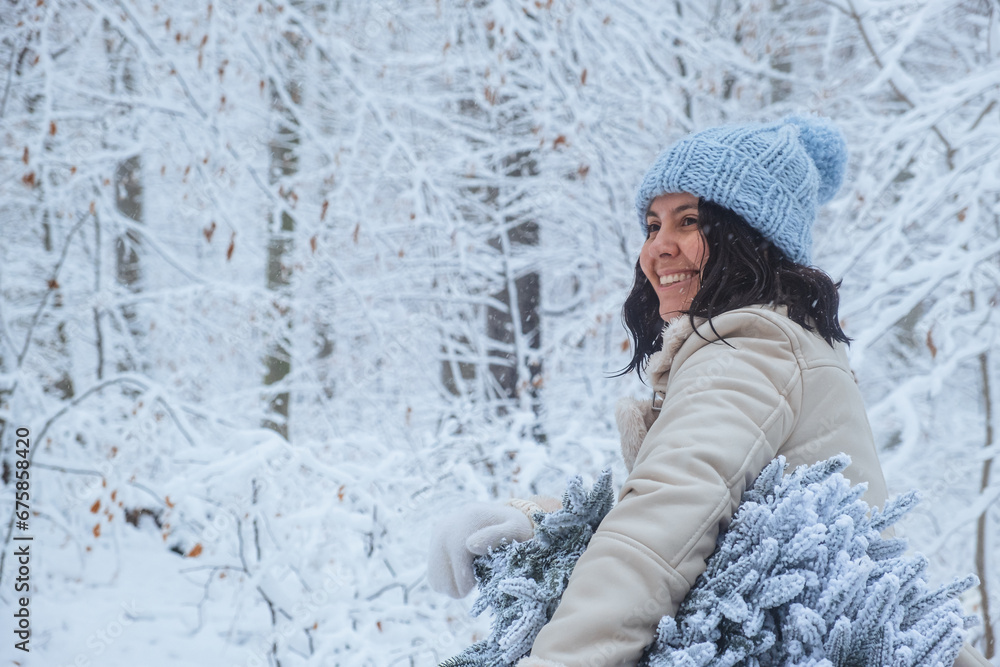 A woman in a winter forest stands holding a snowy Christmas tree with a smile on her face A woman in a winter forest stands holding a snowy Christmas tree with a smile on her face