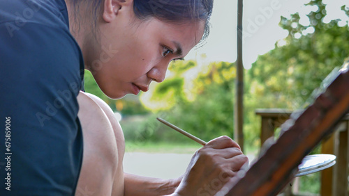 Close-up of Asian woman painter creating art use a paintbrush to draw lettering designs on a wooden coffee shop sign.outdoor activities,People doing activities.