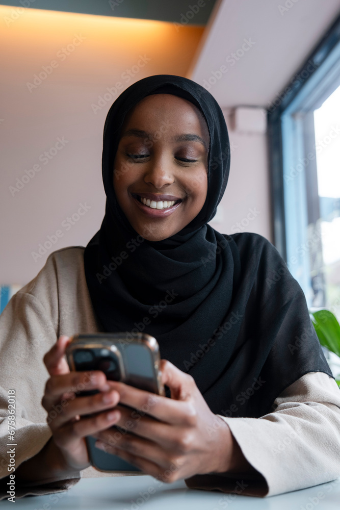 Smiling young woman in hijab using phone in cafe Smiling young woman in hijab using phone in cafe